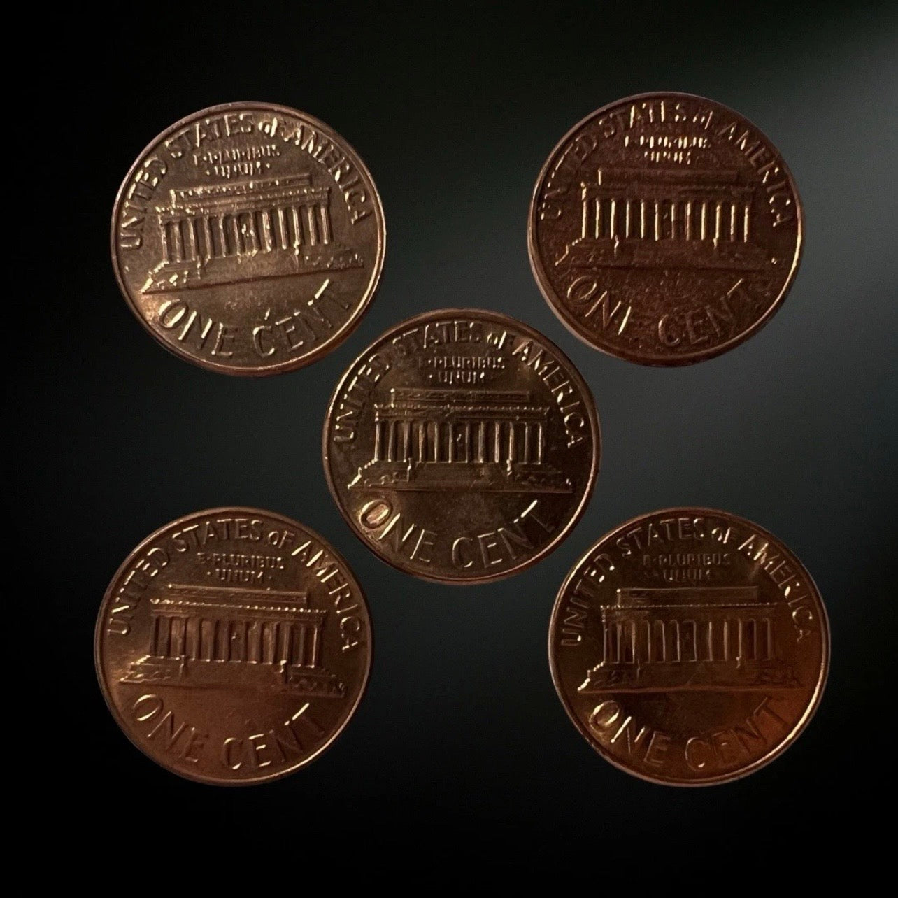 Five pennies from different angles on a dark background